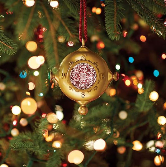A gold ornament hangs from a Christmas tree, symbolizing the spirit of giving in Santa's Kindness Journal.